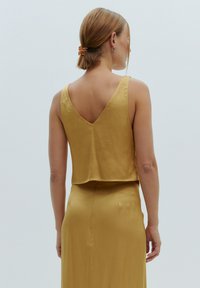 Geel satijnen crop tanktop met een V-back ontwerp, een gladde textuur en brede banden, gedragen met een bijpassende rok.