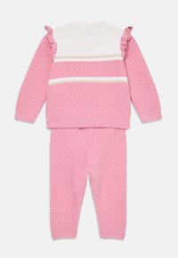Kétrészes kötött ruházat, amely pink pulóverből áll, fehér csíkokkal és fodros részletekkel, párosítva az azték pink nadrággal.