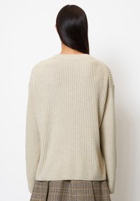 Maglione beige a coste con una vestibilità rilassata, dotato di un ampio scollo e spalle scese. Texture morbida e sottile motivo intrecciato.