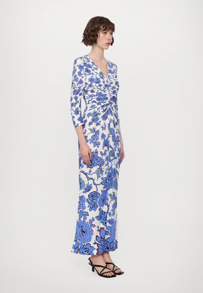 Long floral dress featuring blue and white patterns, a deep V-neckline, three-quarter sleeves, and a ruched waist design. Paired with black sandals.