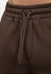 Nahaufnahme von braunen Sweatpants mit elastischem Bund, Zugband und Seitentaschen.