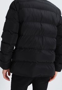 Giacca a vento nera con design trapuntato, caratterizzata da cuciture orizzontali e polsini elasticizzati. Realizzata in materiale leggero e resistente all'acqua.