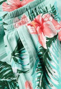 Tissu floral mettant en avant des fleurs rose et rouge avec des feuilles vertes sur un fond menthe clair. Taille élastique avec une texture froncée.