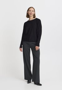 Haut noir à manches longues avec un col bateau et une coupe décontractée, associé à un pantalon large gris foncé et des chaussures noires à bout pointu.