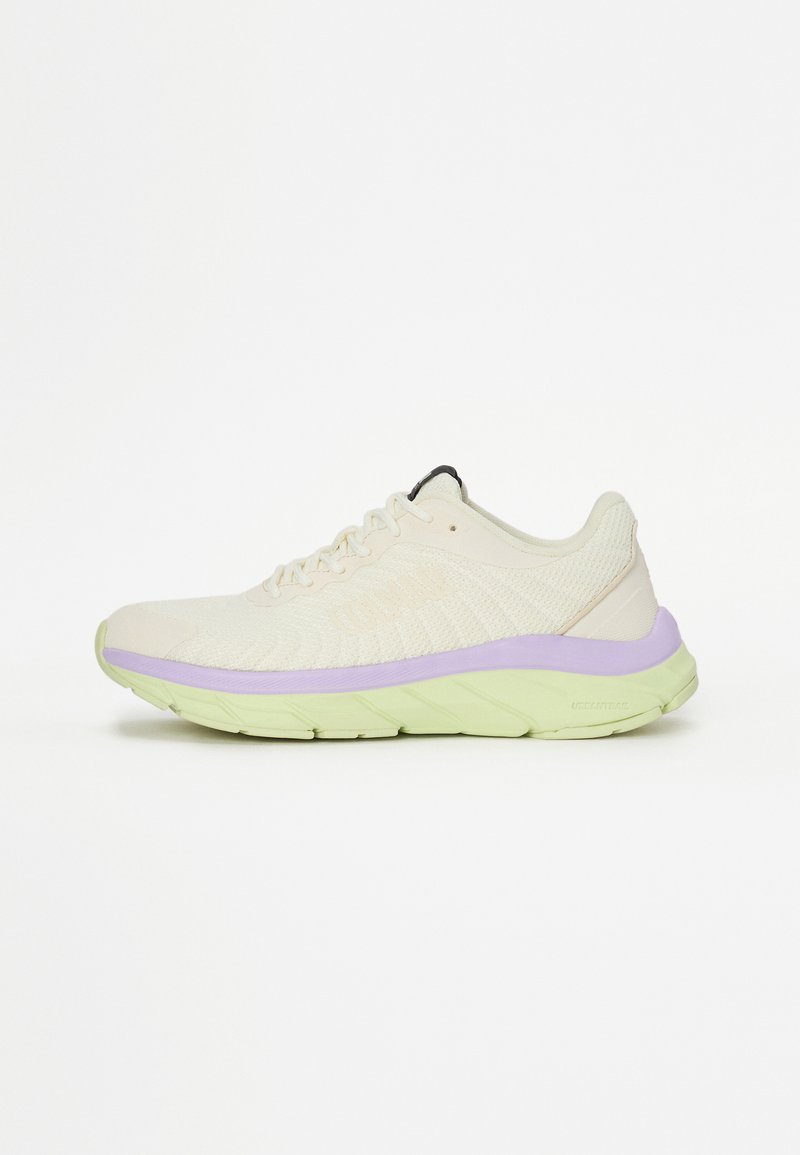 Ανοιχτό μπεζ αθλητικό παπούτσι με υφασμάτινη επάνω επιφάνεια με υφή, μωβ μεσαία σόλα, πράσινη σόλα και μαύρη λεπτομέρεια κοντά στην περιοχή των κορδονιών. Διακρίνεται για την απορρόφηση κραδασμών.