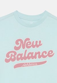 Svijetloplava majica s okruglim izrezom s ružičastim natpisom "New Balance" i rukopisom "Athletics" ispod na prsima.
