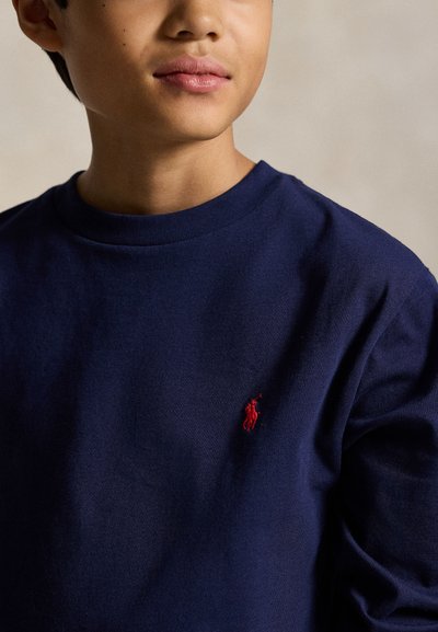 Young person wearing a navy blue sweatshirt with a small red embroidered polo player logo on the chest.