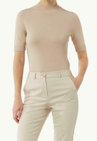 Beige stickad topp med korta ärmar och en ribbad rund halsringning, i kombination med ljusbeiga skräddarsydda byxor med knappstängning.