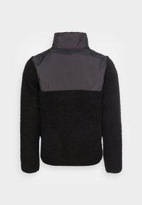 Sort fleecejakke med en kontrasterende grå nylon overdel og høj krave, der har en struktureret yderside og lange ærmer.