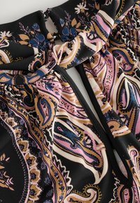 Zwarte stof met een bloemig paisleypatroon in roze, goud en blauw. Heeft een geknoopte detail bij de halslijn en een elastische tailleband.