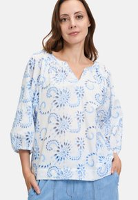 Witte blouse met blauw bloemenpatroon, V-hals en driekwartmouwen. Gemaakt van lichte stof en voorzien van textuuraccenten.