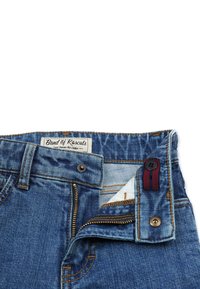 Farkut sinisessä pesussa, kultaisilla tikkauksilla, vetoketjukiinnityksellä ja nappisulkimella. Oleellinen osa on vyötäröllä oleva "Band of Rascals" -merkki.