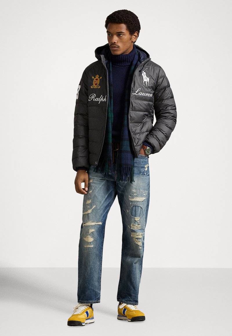 Doudoune noire avec logos brodés, col roulé marine, jean déchiré bleu, et baskets jaunes avec touches de bleu. Tenue texturée et décontractée.