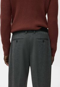 Szare, dopasowane spodnie z tylnymi kieszeniami i czarnymi guzikami, zestawione z dopasowanym, prążkowanym bordowym swetrem. Gładka faktura i uporządkowany krój.