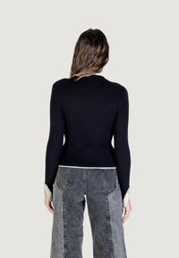 Pull en maille côtelée bleu marine à manches longues, design ajusté, avec un accent blanc en bas, associé à un pantalon en denim ample gris clair.