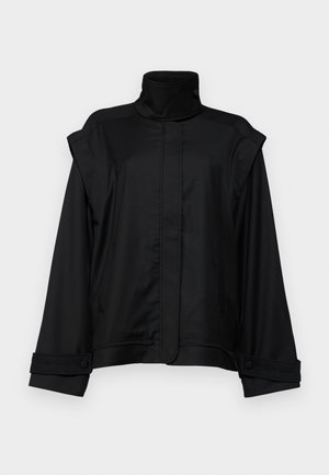 Melna jaka ar augstu apkakli, platām piedurknēm un divām sānu kabatām; izgatavota no gludas auduma, ar pogām aizpogāmām piedurknēm un minimālistisku dizainu.