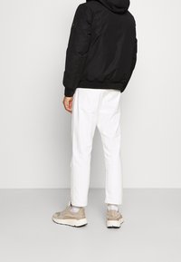 Schwarze gepolsterte Jacke mit Kapuze, gerippten Bündchen, getragen über weißen Hosen, kombiniert mit beigen Sneakers. Einfaches Design und neutrale Farben.