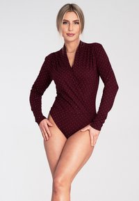 Bordowy body z długim rękawem w białe kropki, o kroju kopertowym, wykonane z gładkiego materiału. Charakteryzuje się wysokim krojem nogawki oraz dopasowaną sylwetką.