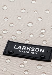 Beige tyg med vattendroppar, med en svart rektangulär etikett där "LARKSON HAMBURG" är präglat med vita bokstäver längst ner.