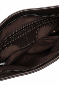 Tumepruun nahast koti sisemus, kus on kangast vooder, lukuga tasku ja õmmeldud brändi silt sees.