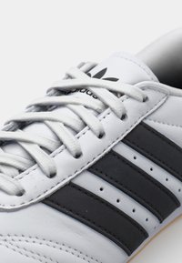 Vita läder sneakers med tre svarta ränder, rund tå och vita snören. Texturerad syntetisk sula och perforeringar för andningsförmåga.