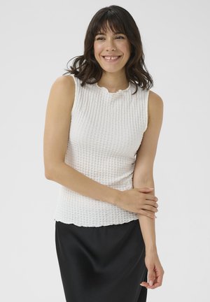 Haut sans manches blanc, texturé, avec un col en forme de scallop, associé à une jupe noire. Le tissu présente un motif à motifs de grille et une silhouette ajustée.