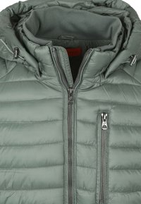 Gevoerde groene jas met een hoge kraag, een rits aan de voorkant en twee zijzakken. De stof heeft een gladde, glanzende textuur met een gewatteerd patroon.