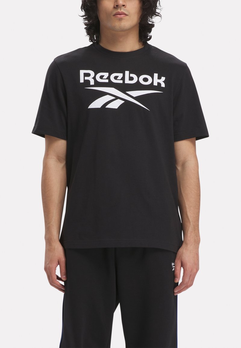 Melnā kokvilnas t-krekliņa ar lielu baltu Reebok logo un stilizētu grafiku. Īsās piedurknes un klasiska apaļa kakla izgriezne.