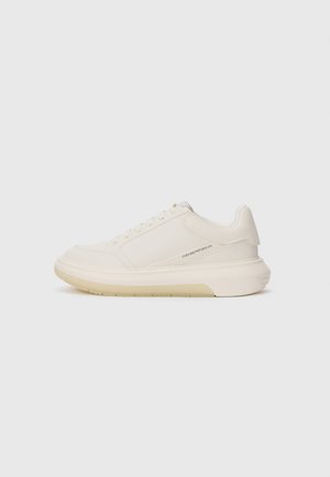 Zapatillas blancas con parte superior de cuero suave, puntera redondeada y suela de goma gruesa. Presentan costuras mínimas y un sutil detalle del logo en el costado.