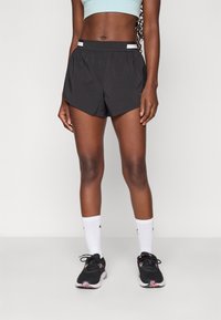Svarta sportshorts med en böjd fåll, med en bred midjeresår och vita ränder. Bärs med svarta löparskor och vita strumpor.