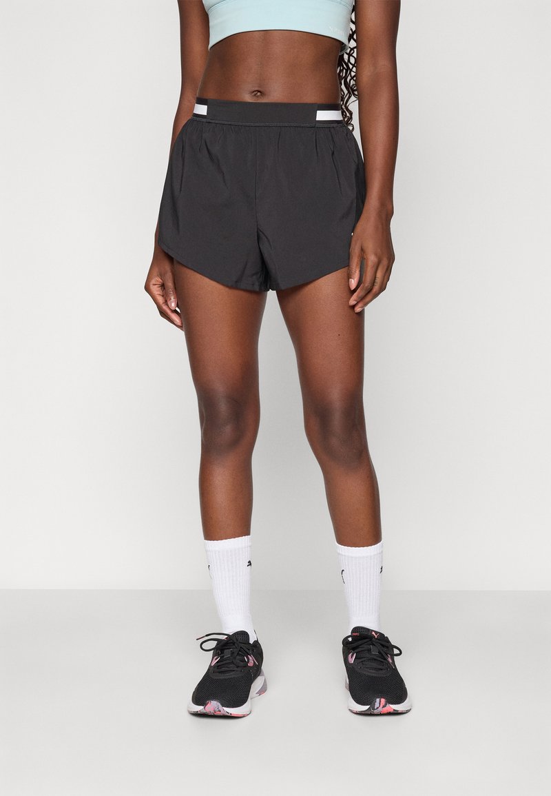 Svarta sportshorts med en böjd fåll, med en bred midjeresår och vita ränder. Bärs med svarta löparskor och vita strumpor.