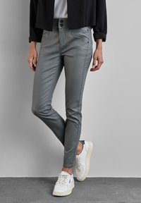 Grå slim-fit byxor i ettslätt tyg; har två framfickor och en dubbelknappad midja, kombinerat med vita sneakers.