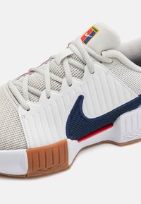 Nike sneaker with a grey mesh upper, white rubber sole, navy blue accents, textured side panels, and multicolored logo on the tongue.