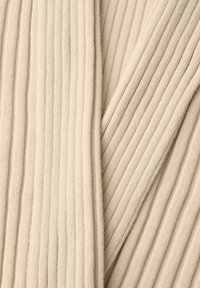 Tissu en maille côtelée beige avec des rainures verticales et une texture douce, présentant des sections pliées formant des lignes diagonales.