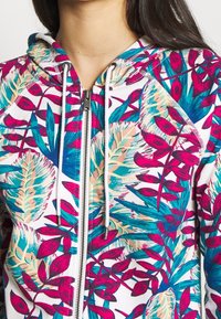 Hooded sweatshirt in white, featuring a vibrant floral pattern in pink, blue, and beige. Silver zipper closure and drawstring details.