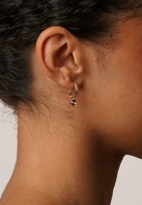 Gul hoopörhänge med en liten mörk ädelsten, med en strukturerad yta och gångjärnsstängning, bärs på örsnibben.