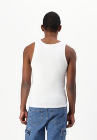 Hvit bomullstopp med rund hals og brede skulderstropper, brukt sammen med blå denim cargo-shorts med lommer.