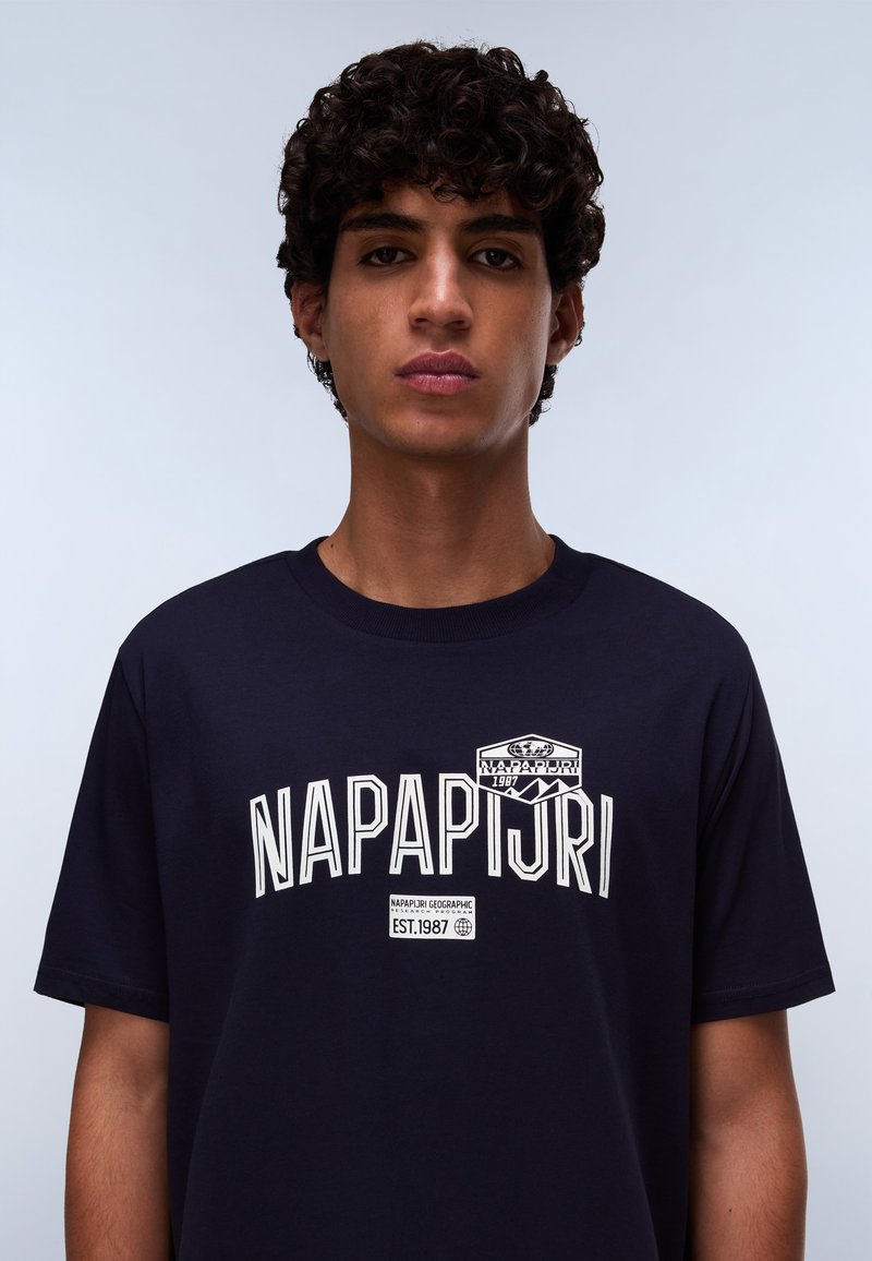 Námorně modré bavlněné tričko s bílým textem "NAPAPIJRI" a logem na horní levé straně. Krátké rukávy a kulatý výstřih. Hladká textura.