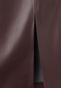 Gros plan sur un tissu en cuir brun foncé lisse avec une ouverture verticale laissant entrevoir un matériau noir en dessous.