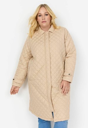 Beige vadderad kappa med krage, framdragkedja och sidofickor. Tyget har en slät textur och är medellång, når knäna.