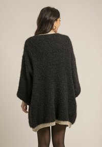 Pull en maille noir surdimensionné avec une texture douce et des manches larges ; présente un ourlet côtelé de couleur claire contrastante en bas.