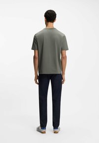 Krótki rękaw zielona oliwkowa koszulka, okrągły dekolt, gładka faktura, w zestawieniu z ciemnymi dżinsami, o prostym kroju nogawki.