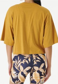 Musztardowa krótka koszulka z szerokimi rękawami, zestawiona z granatowymi szortami z delikatnym kwiatowym wzorem. Miękki, przewiewny materiał bawełniany.