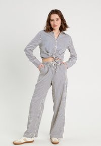 Ensemble de pyjama rayé comprenant une chemise courte nouée avec bouton sur le devant et manches longues, assortie à un pantalon large et des baskets décontractées.
