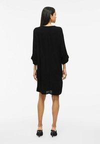 Robe noire avec des manches trois-quarts, coupe ample, mi-longue, fabriquée en tissu doux. Présente un col rond et un design simple.