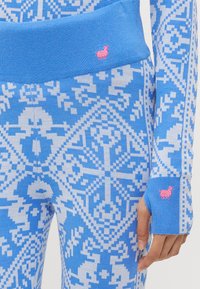 Blå mønstrede strikkede leggings med intrikate hvite geometriske design. Inkluderer et rosa brodert dyr ved midjen og mansjetten.