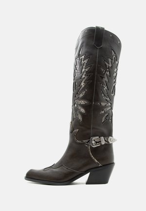 Cizmă de cowboy din piele neagră, cu decupaje decorative, cataramă argintie și toc înclinat, prezentată pe un fundal alb.