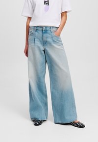 Jeans in denim blu chiaro a gamba larga con una finitura sbiadita, design a cinque tasche, cuciture visibili e vita alta, abbinati a ballerine nere con borchie.