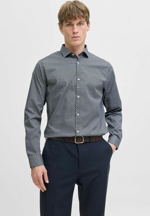 Dunkelblausse Button-up-Hemd mit geometrischem Muster, langen Ärmeln und Kragen; kombiniert mit dunklen Hosen und einem braunen Gürtel.