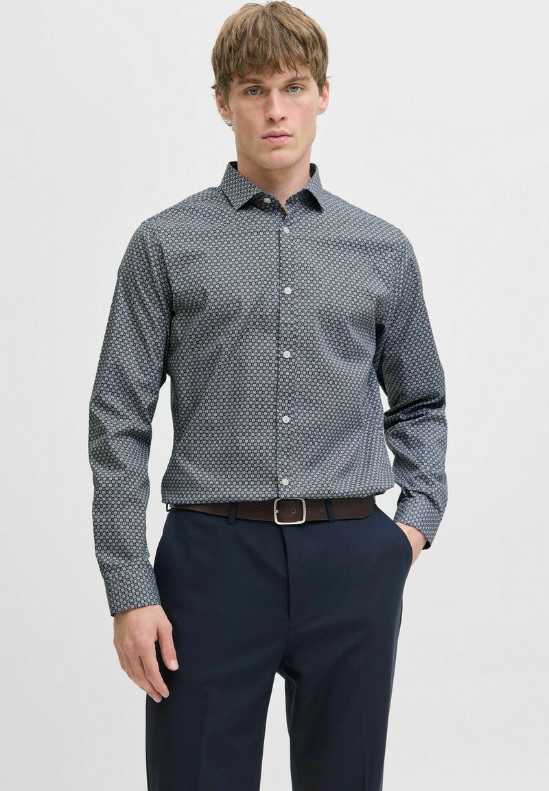 Cămașă cu nasturi de culoare albastru închis, cu un model geometric, mâneci lungi și guler; asortată cu pantaloni negri și o curea maro.